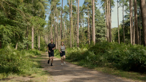 Mid-Adult-Couple-Exercising-Doing-Work-Out-Outdoors-Running-Along-Track-Through-Forest-Towards-Camera-Wearing-Sports-Clothing-Shot-In-Real-Time-1